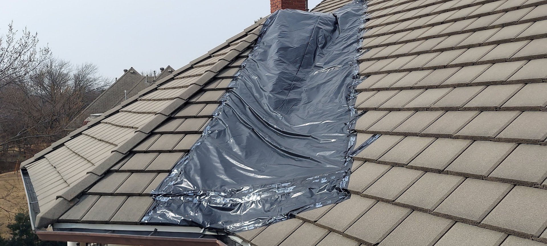 A concrete tile roof with a strip of temporary cover laid down the slope